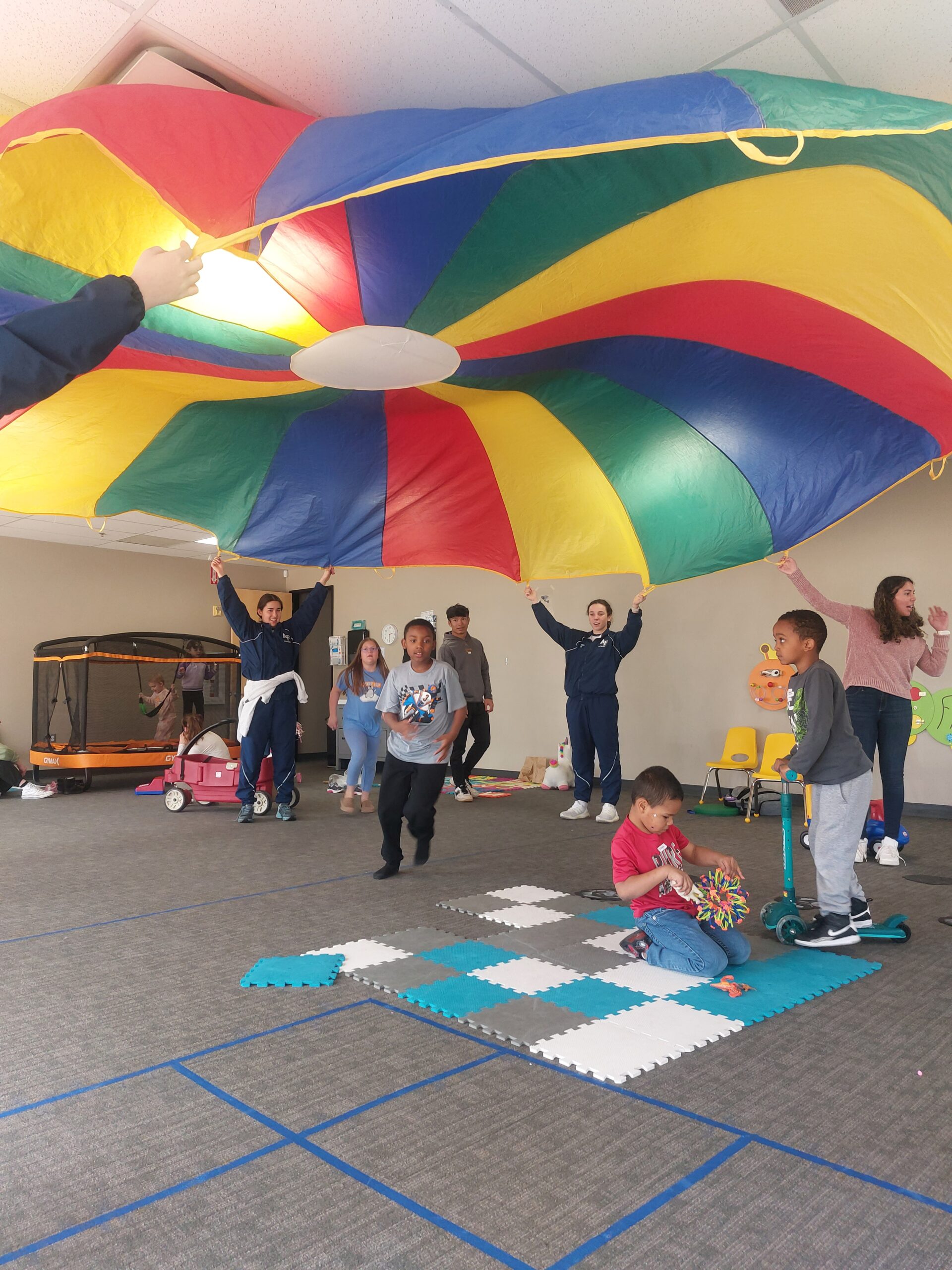 children play indoors with a large colorful parachute