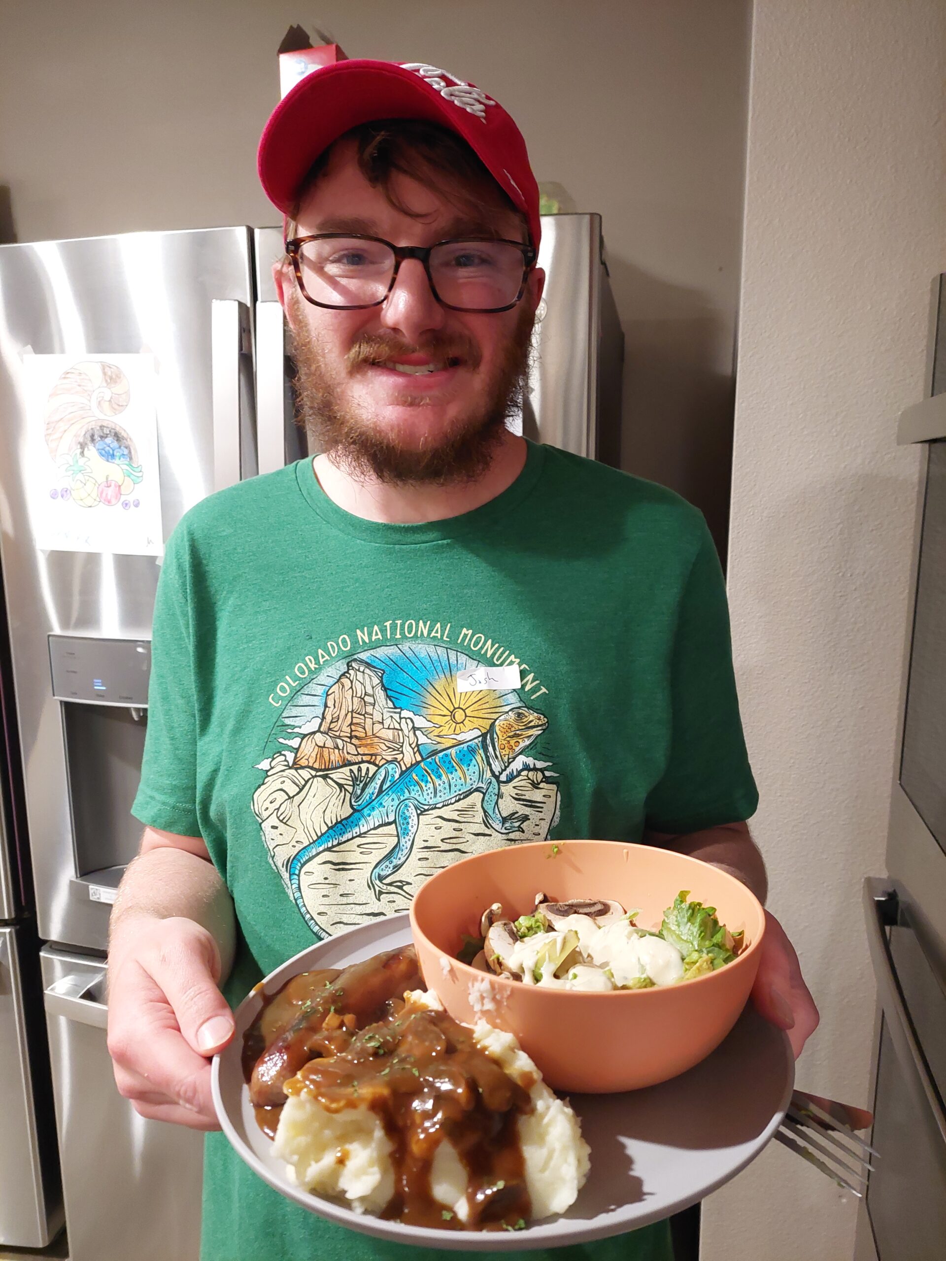 young adult stands smiling at the viewer wearing a green shirt holding a plate of food