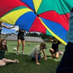 Children playing underneath large colorful parachute tarp