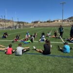 Kids sitting in circle on soccer field stretching